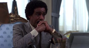 Movie still from “Brewster's Millions” (1985), directed by Walter Hill – A man in a suit and tie sitting in a chair; Close Up shot, Over the shoulder angle