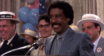 Movie still from “Brewster's Millions” (1985), directed by Walter Hill – A man and a woman smile at a microphone; Close Up shot, Low angle