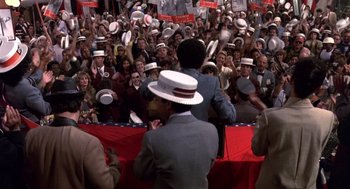 Movie still from “Brewster's Millions” (1985), directed by Walter Hill – A large crowd of people are gathered around a podium; Medium shot, High angle