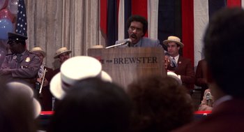 Movie still from “Brewster's Millions” (1985), directed by Walter Hill – A man is speaking at a political event; Medium shot, Low angle