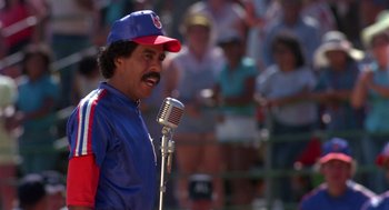 Movie still from “Brewster's Millions” (1985), directed by Walter Hill – A man in a baseball cap is holding a microphone; Medium shot, Low angle