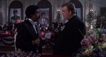 Movie still from “Brewster's Millions” (1985), directed by Walter Hill – Two men in suits talking to each other in front of a crowd of onlookers; Medium shot, Low angle