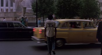 Movie still from “Brewster's Millions” (1985), directed by Walter Hill – A man walking down the street in front of a yellow taxi cab; Wide shot, Over the shoulder angle