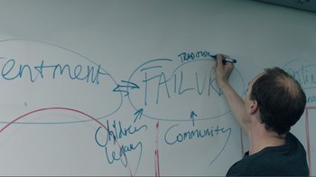 Movie still from “Brexit” (2019), directed by Toby Haynes – A person writing on a wall with a white board; Medium shot, High angle