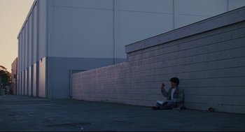 Movie still from “Brick” (2005), directed by Rian Johnson – A person sitting on the ground in front of a wall; Wide shot, Low angle