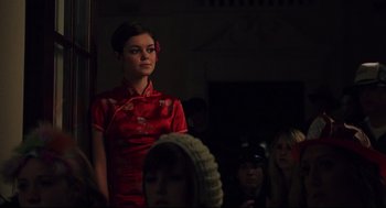 Movie still from “Brick” (2005), directed by Rian Johnson – A woman in a red dress standing in front of a group of people; Medium shot, Over the shoulder angle
