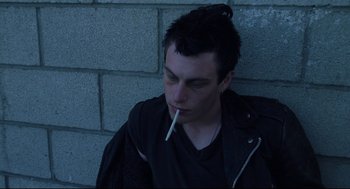 Movie still from “Brick” (2005), directed by Rian Johnson – A man sitting on the side of a wall with a cigarette in his mouth; Close Up shot, High angle