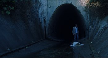Movie still from “Brick” (2005), directed by Rian Johnson – A man standing next to a body in a tunnel; Wide shot, High angle