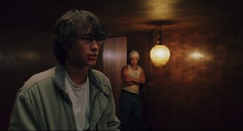 Movie still from “Brick” (2005), directed by Rian Johnson – Two young men standing in a dimly - lit room; Medium shot, Over the shoulder angle