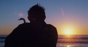 Movie still from “Brick” (2005), directed by Rian Johnson – A man with an umbrella looking out over the ocean at sunset; Medium shot, Low angle