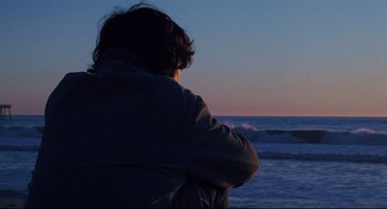 Movie still from “Brick” (2005), directed by Rian Johnson – A person sitting on the beach looking out at the ocean; Medium shot, Low angle