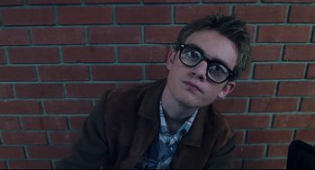 Movie still from “Brick” (2005), directed by Rian Johnson – A young man wearing glasses sitting against a brick wall; Close Up shot, Low angle