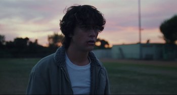 Movie still from “Brick” (2005), directed by Rian Johnson – A young man is standing in a field at sunset; Close Up shot, Over the shoulder angle