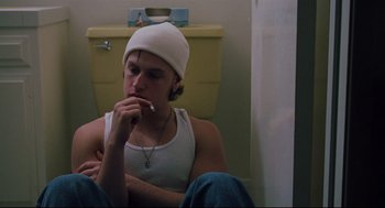 Movie still from “Brick” (2005), directed by Rian Johnson – A man sitting in a bathroom with a cigarette in his mouth; Medium shot, Low angle