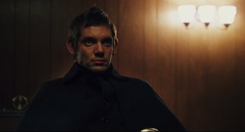 Movie still from “Brick” (2005), directed by Rian Johnson – A man wearing a black coat standing next to a wall; Close Up shot, High angle