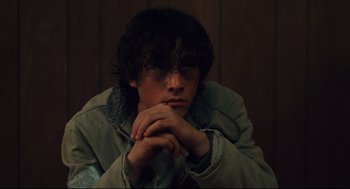 Movie still from “Brick” (2005), directed by Rian Johnson – A young man sitting in front of a wooden wall with his hands crossed; Close Up shot, High angle