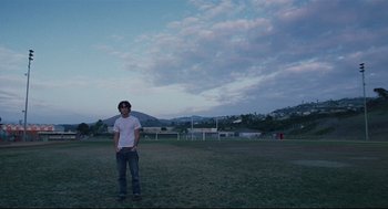 Movie still from “Brick” (2005), directed by Rian Johnson – A man standing in a field holding a frisbee; Wide shot, Low angle