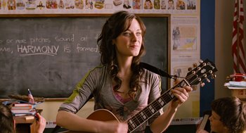 Movie still from “Bridge to Terabithia” (2007), directed by Gabor Csupo – A woman sitting in front of a chalkboard holding a guitar; Close Up shot, Over the shoulder angle