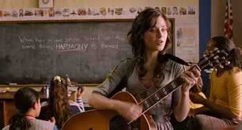 Movie still from “Bridge to Terabithia” (2007), directed by Gabor Csupo – A woman holding a guitar in front of a chalkboard; Medium shot, Over the shoulder angle