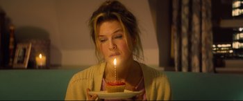 Movie still from “Bridget Jones's Baby” (2016), directed by Sharon Maguire – A woman blowing out a candle on a cupcake on a plate; Close Up shot, Overhead angle