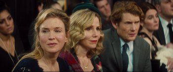 Movie still from “Bridget Jones's Baby” (2016), directed by Sharon Maguire – Two women and a man are sitting in a crowd; Close Up shot, Over the shoulder angle