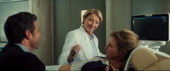 Movie still from “Bridget Jones's Baby” (2016), directed by Sharon Maguire – A female dentist is smiling as a female patient looks on; Medium shot, Over the shoulder angle