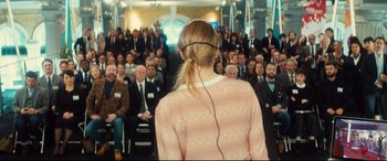 Movie still from “Bridget Jones's Baby” (2016), directed by Sharon Maguire – A crowd of people sitting in front of a woman wearing headphones; Medium shot, Over the shoulder angle