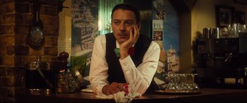 Movie still from “Bridget Jones's Baby” (2016), directed by Sharon Maguire – A man sitting at a table in front of a painting; Close Up shot, Low angle