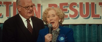 Movie still from “Bridget Jones's Baby” (2016), directed by Sharon Maguire – An older woman is holding a microphone in front of a man; Close Up shot, Over the shoulder angle