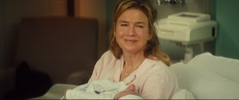 Movie still from “Bridget Jones's Baby” (2016), directed by Sharon Maguire – A woman in a pink shirt is holding a baby; Close Up shot, Over the shoulder angle