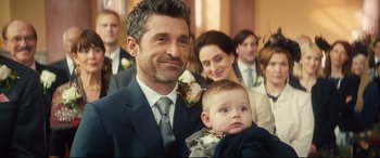 Movie still from “Bridget Jones's Baby” (2016), directed by Sharon Maguire – A man in a suit holding a baby in his arms; Close Up shot, Over the shoulder angle