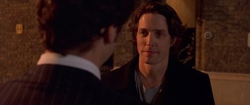 Movie still from “Bridget Jones's Diary” (2001), directed by Sharon Maguire – A man with long dark hair is talking to another man; Close Up shot, Over the shoulder angle