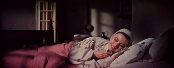 Movie still from “Brigadoon” (1954), directed by Vincente Minnelli – A woman laying on a bed with her eyes closed and holding a cell phone; Medium shot, Overhead angle