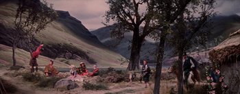 Movie still from “Brigadoon” (1954), directed by Vincente Minnelli – A group of people sitting on the ground next to a tree; Extreme Wide shot, High angle