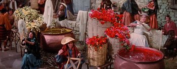 Movie still from “Brigadoon” (1954), directed by Vincente Minnelli – A group of people sitting around some baskets of flowers; Wide shot, High angle