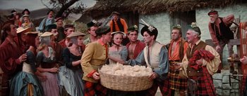 Movie still from “Brigadoon” (1954), directed by Vincente Minnelli – A group of people standing next to each other holding a basket; Medium shot, High angle