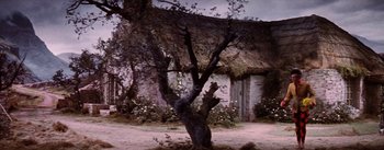 Movie still from “Brigadoon” (1954), directed by Vincente Minnelli – A tree in front of a house with a thatched roof; Wide shot, Low angle