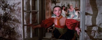 Movie still from “Brigadoon” (1954), directed by Vincente Minnelli – A woman in a red and black dress is looking out of a window; Medium shot, Over the shoulder angle