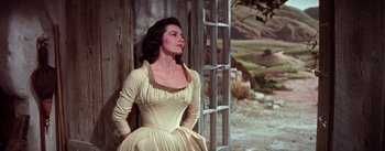 Movie still from “Brigadoon” (1954), directed by Vincente Minnelli – A woman in a white dress standing in front of a wooden fence; Medium shot, Low angle