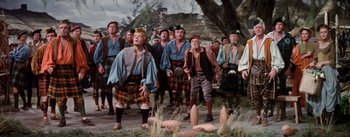 Movie still from “Brigadoon” (1954), directed by Vincente Minnelli – A group of men standing next to each other on a dirt road; Wide shot, Low angle