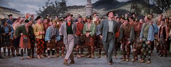 Movie still from “Brigadoon” (1954), directed by Vincente Minnelli – A group of men in suits and hats in front of a crowd; Medium shot, Low angle