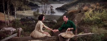 Movie still from “Brigadoon” (1954), directed by Vincente Minnelli – A man and a woman sitting on a log near a body of water; Wide shot, High angle