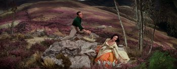 Movie still from “Brigadoon” (1954), directed by Vincente Minnelli – A man and a woman are sitting on a rock; Wide shot, High angle