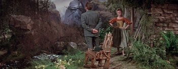 Movie still from “Brigadoon” (1954), directed by Vincente Minnelli – A man and a woman standing next to a wooden chair; Wide shot, High angle