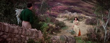 Movie still from “Brigadoon” (1954), directed by Vincente Minnelli – A woman walking down a dirt path near a field; Wide shot, High angle