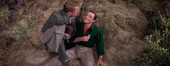 Movie still from “Brigadoon” (1954), directed by Vincente Minnelli – Two men sitting on the ground with one holding a cell phone; Medium shot, High angle