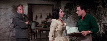 Movie still from “Brigadoon” (1954), directed by Vincente Minnelli – A woman in a dress standing next to a table; Medium shot, Over the shoulder angle