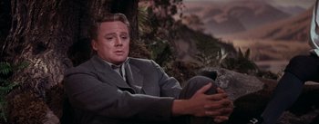 Movie still from “Brigadoon” (1954), directed by Vincente Minnelli – A man sitting on the ground in front of a tree; Medium shot, Low angle