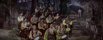 Movie still from “Brigadoon” (1954), directed by Vincente Minnelli – A large group of men in medieval garb are posing for a picture; Wide shot, High angle