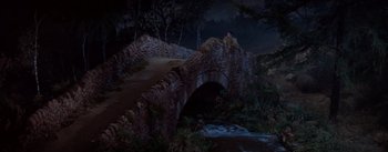 Movie still from “Brigadoon” (1954), directed by Vincente Minnelli – A man sitting on top of a bridge over a river; Extreme Wide shot, High angle